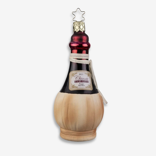 A Christmas ornament shaped like a cognac bottle, featuring a light wood-grained base, a dark glass neck, a metallic red top, and a gold star finial, set against a plain light gray background.