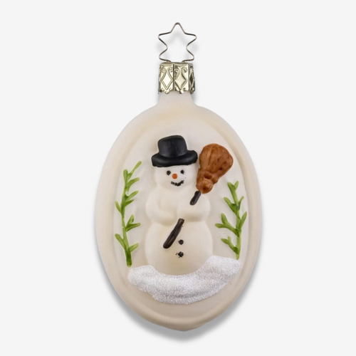 An oval glass Christmas ornament featuring a hand-painted snowman wearing a black top hat and holding a brown broom, standing on white snow with green sprigs, set against a light gray background.
