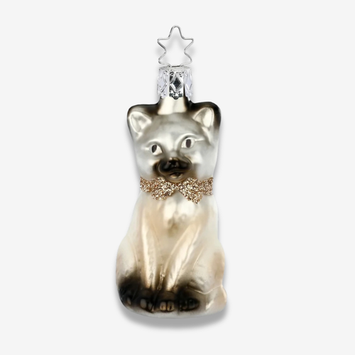 A decorative cat-shaped ornament with a glossy silver and cream body, dark brown tips, and a glittery gold bow tie, topped with a clear faceted crystal and a silver star.