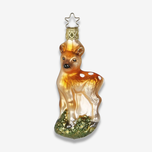 A decorative glass ornament shaped like a fawn, with a warm amber-brown body, white spots, and a glittery green base, hanging from a gold star cap on a light gray background.