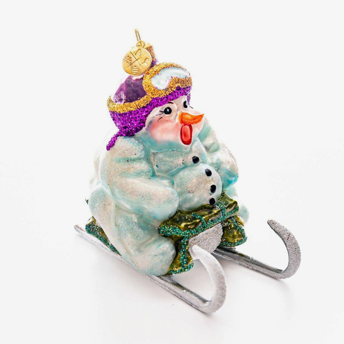 A festive ornament featuring a snowman on a sled with goggles on a white background