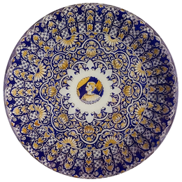 A 13-inch round glass plate featuring an intricate blue and yellow design with a woman in the center. 