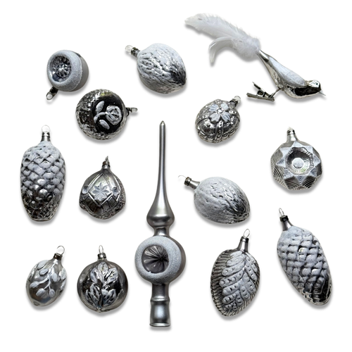 A set of silver-toned Christmas ornaments arranged on a white background, including textured pinecones, faceted balls, a bird ornament with a white feather, and a tall metallic finial.