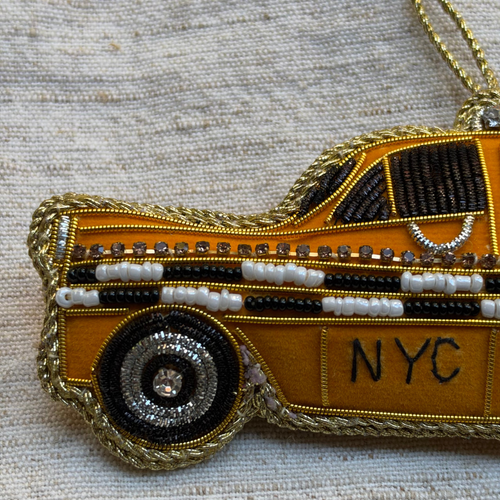 A fabric covered ornament in the shape of a New York City Taxi, with  beads and embroidery on grey background. 