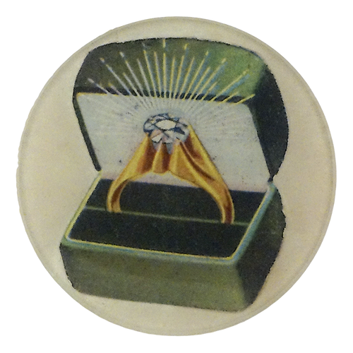 A four inch round plate showing an open green ring box with a gold ring and a large central gemstone, isolated on a light cream background.