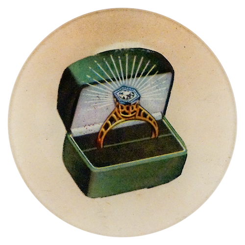 A five inch round handblown glass plate featuring a ring in a green box on a beige background