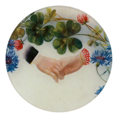 A five inch round glass plate featuring a close up of two people holding hands with flowers and clovers above the hands on a white background. 