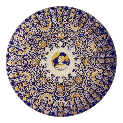 A five inch round glass plate featuring an intricate blue and yellow design. A small sketch of a woman is represented in the center
