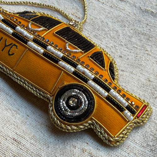 A fabric covered ornament in the shape of a New York City Taxi, with  beads and embroidery on grey background. 