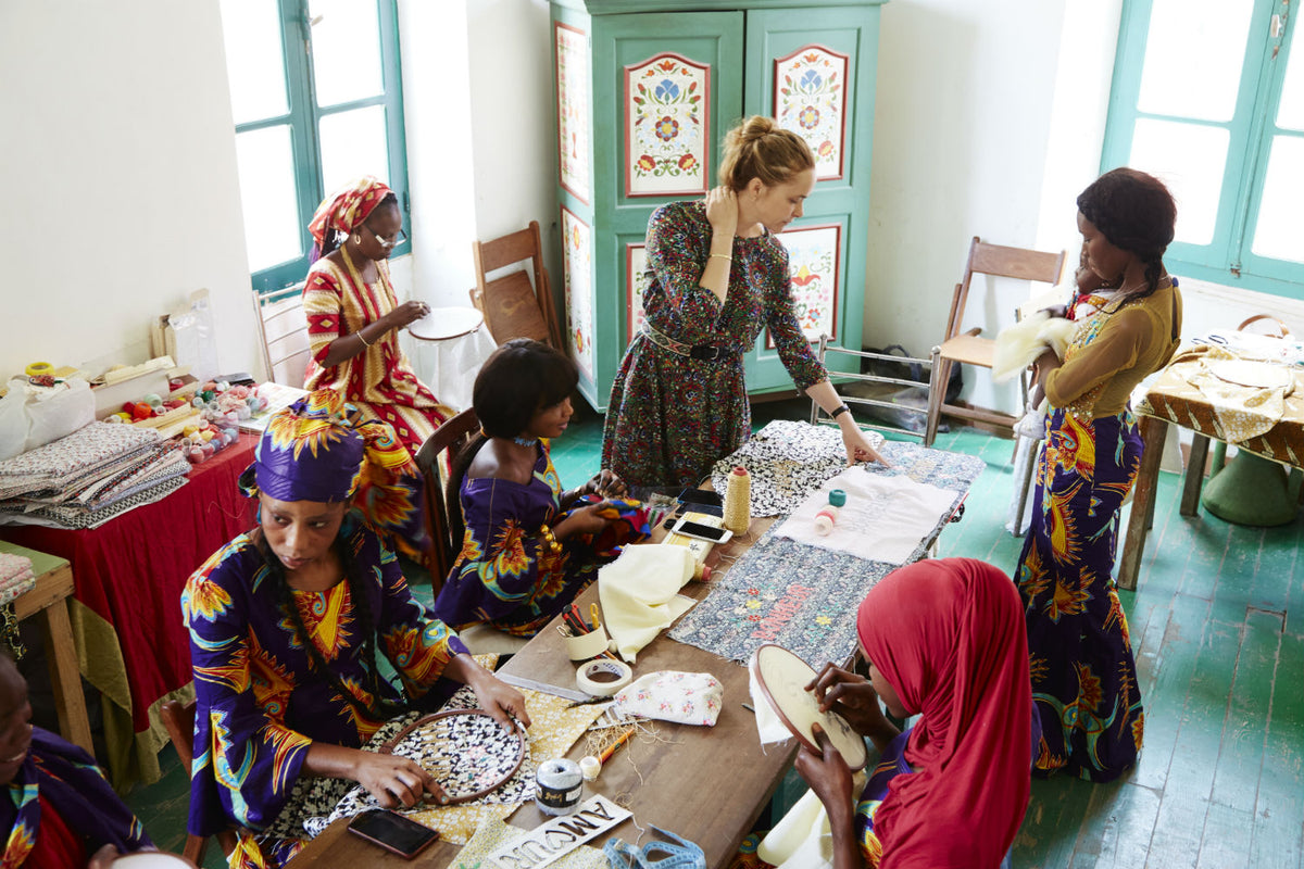 A group of 6 people embroidering fabrics in a sun drenched room