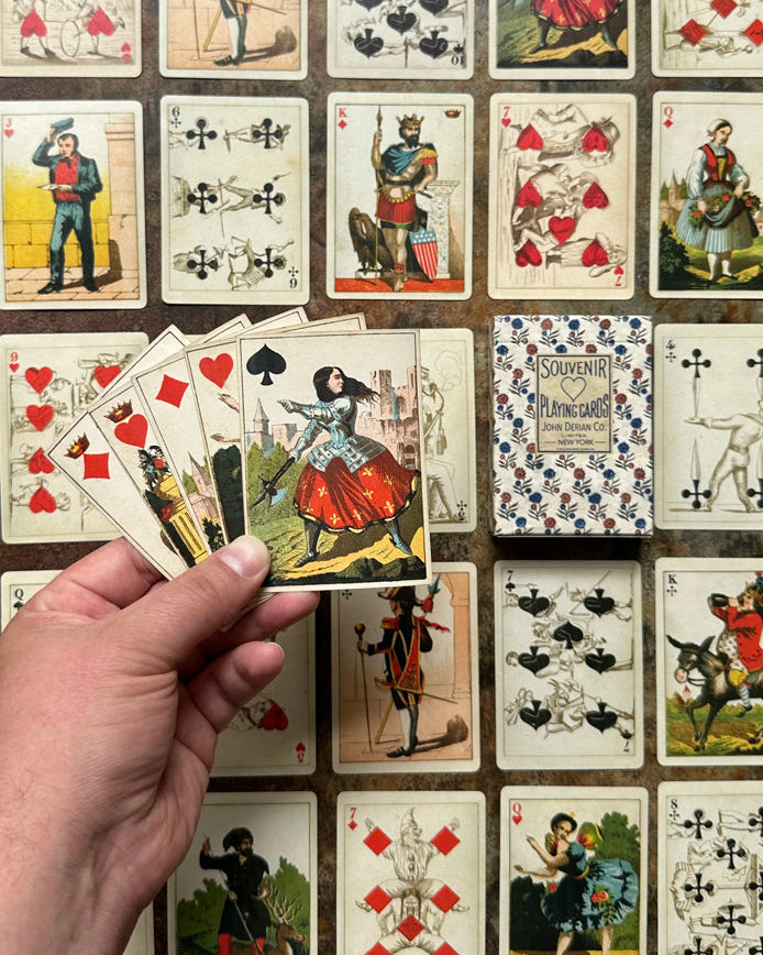 Hand holding vintage playing cards with a grid of additional playing cards in the background.