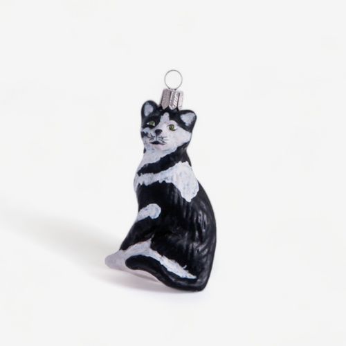 A hand-painted black and white glass Christmas ornament shaped like a sitting cat, complete with a silver hanging loop at the top, set against a plain white background.
