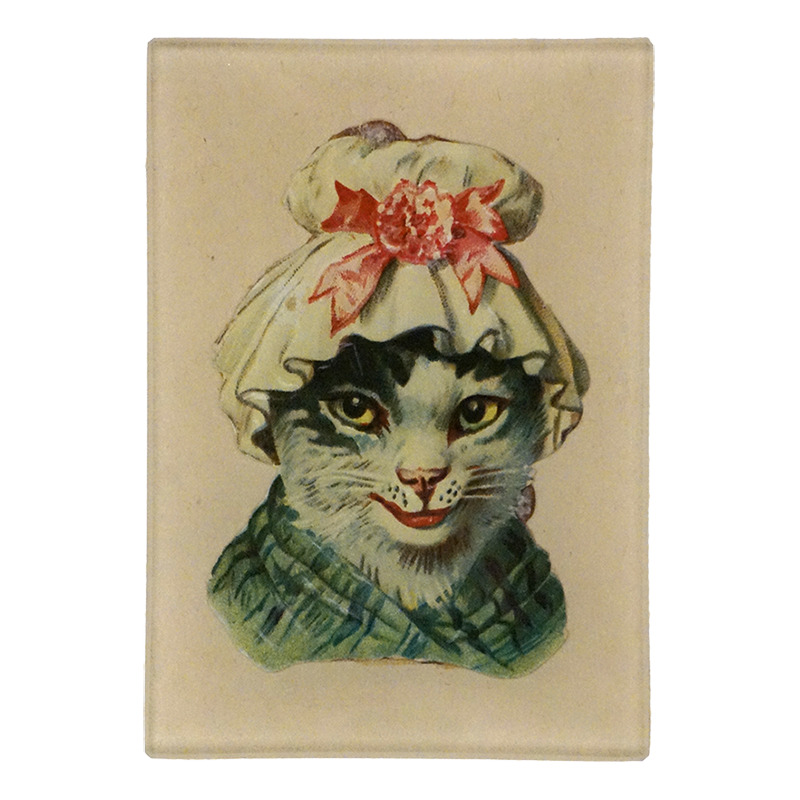 A three and a half inch by five inch vertical glass tray featuring a cat wearing a cream bonnet with a red flower and bow, plus a green scarf, centered on a light beige background.