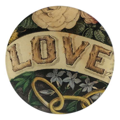 A five inch round glass plate featguring the work 'LOVE' in a font that resemble a wood like feature. Flowers and foliage surround the word. 