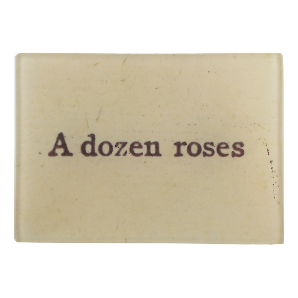 The text 'A dozen roses' written on a beige background on a three and a half inch by five inch glass tray.